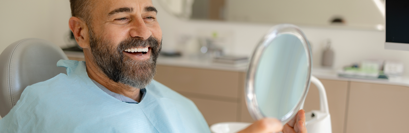 man-smiling-in-mirror-at-dentist-1600x522.png