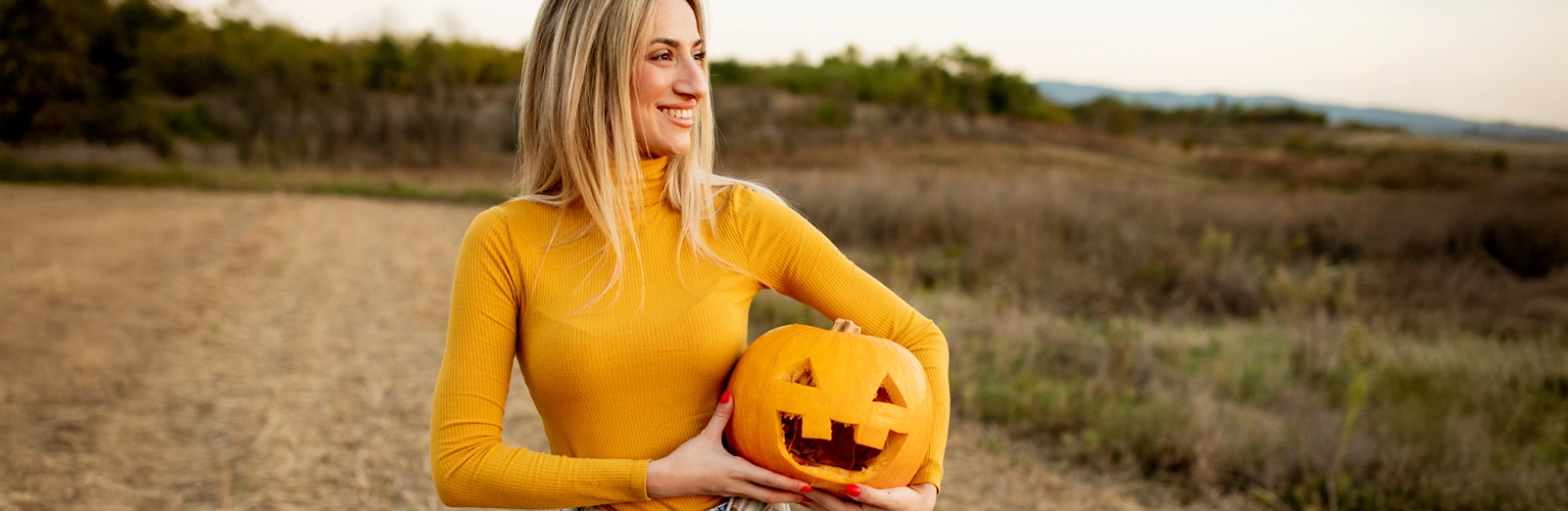 woman-smiling-holding-jack-o-lantern-1600x522.webp