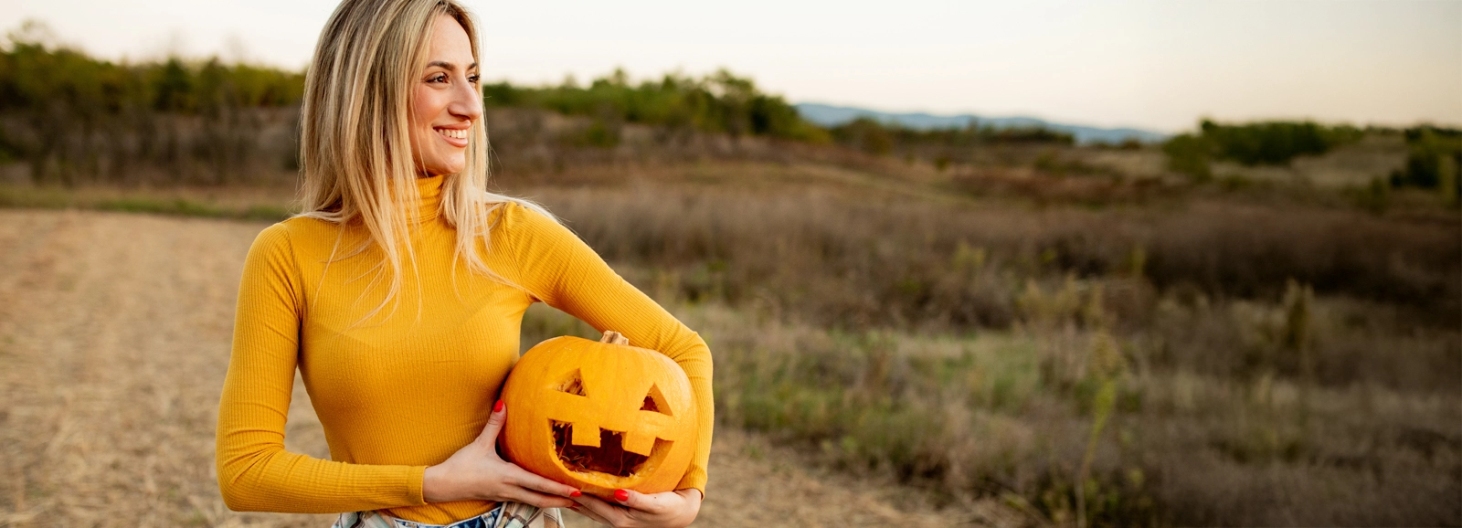 woman-smiling-holding-jack-o-lantern-1600x578.webp