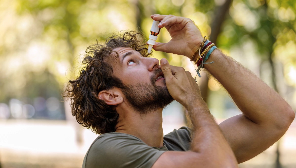 Man outdoors during spring applying eye drops while looking up