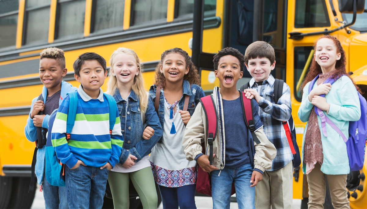 young-students-smiling-by-school-bus-1200x683.webp